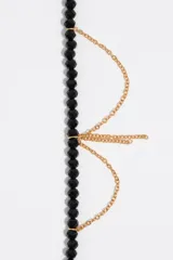 Pulsera de cuentas de cristal facetado negro combinada con finas cadenas doradas colgantes y dije con detalles esmaltados.