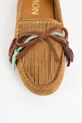 Mocasin de gamuza color camel, con detalle de flecos decorativos en la parte frontal en tonos marrón, violeta y verde agua.
