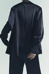 Camisa de manga larga color azul marino, confeccionada en tejido satinado. Presenta cuello solapa, puños anchos y cierre frontal mediante lazada ajustable en el centro.