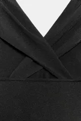 Top negro confeccionado en tejido de punto con escote pico, tirantes anchos cruzados en la espalda, detalle de drapeado en hombros y aplicación de hombreras.