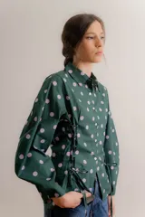 Camisa de popelina con estampado de lunares, cuello clásico y cierre frontal con botones. Presenta un diseño con fruncido lateral tipo corset con cordones ajustables y mangas abullonadas.