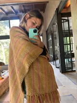 Ruana artesanal color crudo con rayas horizontales color ladrillo y flecos.