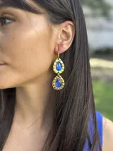 Aros colgantes dorados con dos gemas facetadas en forma de lágrima color azul zafiro.