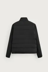 Campera acolchada negra de cuello alto, con cuerpo matelasseado y mangas lisas de tejido elástico. Cuenta con bolsillos en las caderas, cierre frontal por cremallera y bajo con elástico.