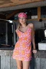 Vestido corto con escote en V y breteles finos, confeccionado en una mezcla de lino y algodón. Presenta un estampado floral vibrante en tonos naranja, rosa y blanco, con un corte relajado que se ajusta suavemente al cuerpo y un pequeño tajo lateral en el ruedo.