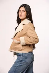 Campera tipo gamulán de gamuza color tostado con interior y solapas de corderito sintético color crema. Presenta cierre frontal con botones, bolsillos cuadrados delanteros y detalles de costuras visibles.