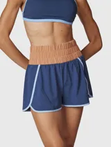 Short deportivo 2 en 1 de color azul con detalles en celeste, que incluye una calza interior incorporada. Presenta una cintura ancha elástica en color tostado, bolsillos laterales y traseros, y está confeccionado con tecnología de secado rápido.