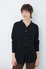 Cardigan de punto color negro, con cuello camisero, cierre frontal con botones y un bolsillo aplicado en el pecho. Presenta mangas largas con puños ajustados.