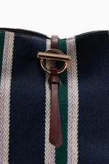 Cartera bombonera con estampado a rayas en tonos azul marino, verde y blanco, con detalles de asa y correa ajustable en material sintético marrón oscuro. Cuenta con cierre de trabilla con herraje metálico en la parte superior.