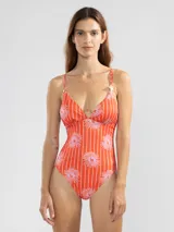 Traje de baño enterizo de lycra color naranja con rayas verticales blancas y estampado de flores rosas. Tiene escote en V, breteles finos y charms florales en los tirantes.