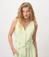 Chaleco de crepe color verde menta con escote en V profundo, sin mangas, bolsillos o falsas solapas con botones dorados y ruedo asimétrico en punta.