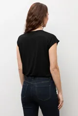 Blusa blanca de manga corta y corte recto, con escote bote y detalle metálico circular en el hombro.