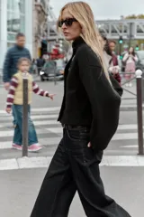 Chaqueta estilo bomber de punto color negro, con cuello subido, manga larga y cierre frontal cruzado con botones ocultos a presión. Presenta bolsillos delanteros de vivo.
