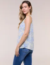 Blusa de lino y rayón color beige con estampado floral en tonos celestes, sin mangas, con escote redondo y detalle de tres aros metálicos plateados entrelazados en el frente.