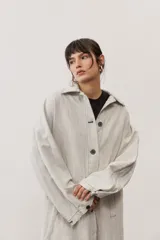 Chaqueta oversize de gabardina color verde claro, con solapa clásica, bolsillos frontales, cierre de botones oscuros y mangas largas con vuelta en tono verde lima vibrante.