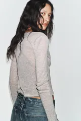 Chaqueta de punto color beige con escote en pico y manga larga, que incluye un top interior integrado con detalle de encaje a tono. Cierre frontal mediante botones.