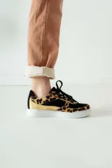 Championes de diseño urbano con estampado animal print de leopardo, combinados con paneles de gamuza negra y detalles en cuero metalizado dorado. Presentan suela blanca plana y cordones negros.