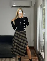 Pollera midi de corte recto con tajo lateral, confeccionada en tela con estampado escocés en tonos marrones, blancos y negros.