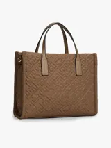 Cartera tipo tote de Tommy Hilfiger, confeccionada en nailon reciclado color marrón con diseño acolchado de monograma TH. Cuenta con dos asas superiores, cierre de cremallera y logo metálico distintivo en la parte frontal.