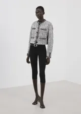 Chaqueta de tweed en tonos gris y blanco, con cuello redondo, manga larga, bolsillos frontales de ribete y cierre delantero con botones.