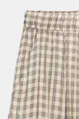 Pantalón de tiro medio con diseño de cuadros vichy en tonos neutros. Presenta pierna ancha, cintura elástica ajustable con cordones, bolsillos laterales y detalle de pinzas en el delantero.
