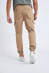Pantalón cargo color beige con ajuste slim, cierre frontal con botón, bolsillos laterales tipo cargo y puños elásticos en los tobillos.