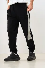 Pantalón negro de corte deportivo con cintura elástica y cordón ajustable. Presenta una franja vertical gris a lo largo de la pierna y puños elásticos.