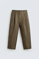 Pantalón de corte relajado confeccionado en mezcla de algodón y lino, con diseño de pliegues frontales, bolsillos laterales y bolsillos traseros de vivo. Presenta cierre frontal con cremallera y botón, con un acabado de lavado especial que le otorga una apariencia única.