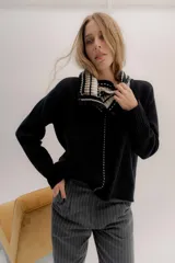 Polera tejida en lambswool color beige, con cuello alto y diseño de intarsia en tonos marrones y grises. Presenta botones forrados en el cuello para modular la apertura.