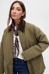 Campera de gabardina color marrón con cuello de pana en tono oscuro. Presenta cierre frontal con botones a presión, bolsillos laterales con solapa y diseño de calce clásico.