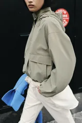 Cazadora de cuello subido con capucha ajustable, manga larga con puños elásticos y bolsillos delanteros con solapa. Presenta bajo elástico y cierre frontal con cremallera oculta y botones a presión.
