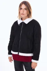 Campera de estilo aviador en color negro, confeccionada en material tipo gamuza con interior y bordes de corderito blanco. Presenta cierre frontal, cuello con solapas y hebilla metálica decorativa.