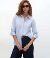 Camisa de tricolina de algodón con estampa de rayas celestes y blancas, cuello solapa, abotonado frontal y mangas largas. Marca Cortelle.