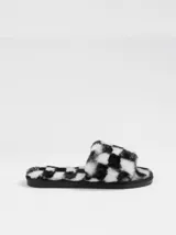 Pantuflas de estilo slide confeccionadas en material sintético de pelo largo con estampado a cuadros en blanco y negro. Presentan una suela plana de goma antideslizante.