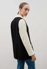 Blazer de lana con diseño bicolor, cuerpo en color negro y mangas en color crema. Presenta un corte holgado, cierre cruzado con doble botonadura y solapas amplias en contraste.