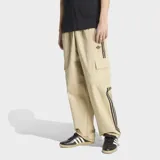 Pantalón cargo Adidas de corte holgado, color beige, confeccionado en tejido antidesgarre. Presenta las icónicas tres rayas laterales en negro, bolsillos cargo en los laterales y logo del trifolio bordado en la pierna izquierda.