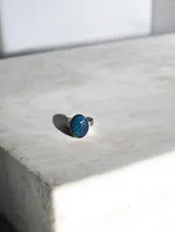 Anillo de acero quirúrgico con piedra ovalada de color azul profundo con vetas craqueladas.