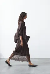 Camisa negra de corte relajado y caída fluida, con cuello clásico, escote en V y cierre frontal con botones forrados. Presenta mangas largas con puños abotonados.