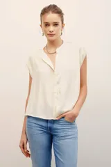 Camisa sin mangas de corte amplio y color fucsia, con cuello mao y cierre frontal de botones ocultos.