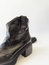 Botas texanas negras de cuero charol con caña baja, punta fina y tacón cuadrado.