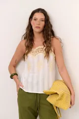 Musculosa blanca de tirantes finos con detalle de encaje y bordados en tono amarillo pastel en la parte superior y frontal.