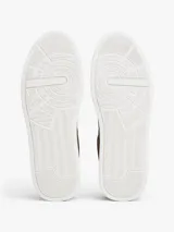Zapatillas de corte bajo Tommy Hilfiger confeccionadas en una combinación de piel nobuk y piel lisa en color marrón. Presentan suela de goma blanca, detalle de ventilación lateral, logo de la marca en la lengüeta, lateral y talón, y cierre mediante cordones.