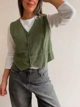 Chaleco de pana fina color verde oliva, con escote en V, cierre frontal de botones y corte entallado.
