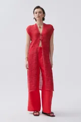 Kimono tejido de punto en color crudo con sutil brillo de lurex. Presenta un diseño sin mangas, corte largo y cierre frontal mediante dos lazos finos. El tejido tiene una textura acanalada vertical.