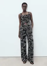 Pantalón de tiro medio confeccionado en mezcla de lino y viscosa, con diseño recto, bolsillos laterales, trabillas y cierre de botón y cremallera. Presenta un estampado de flores y hojas de estilo lineal en contraste.