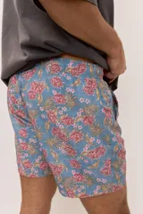 Short de baño celeste con estampa tropical de flores, cintura con cordón ajustable y detalle de etiqueta textil en el lateral.