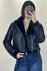 Campera tipo aviador de cuero sintético negro con interior y detalles de piel sintética al tono en cuello, puños y ruedo. Presenta cierre frontal cruzado y cinturón ajustable con hebilla metálica en la cintura.