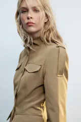 Cazadora de estilo militar en color tostado, con cuello subido, cierre frontal con botones y múltiples bolsillos con solapa en el pecho y la cintura. Cuenta con mangas largas con trabillas en los hombros.