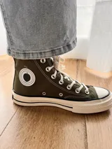 Zapatillas de lona color beige, tipo bota, con cordones marrones, puntera de goma y logo de peach engomado.