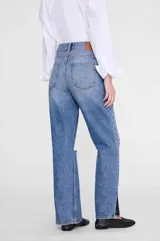 Pantalón jean de tiro alto y pierna recta amplia, color azul medio con efecto lavado. Presenta detalles de roturas sutiles a la altura de las rodillas y diseño clásico de cinco bolsillos.